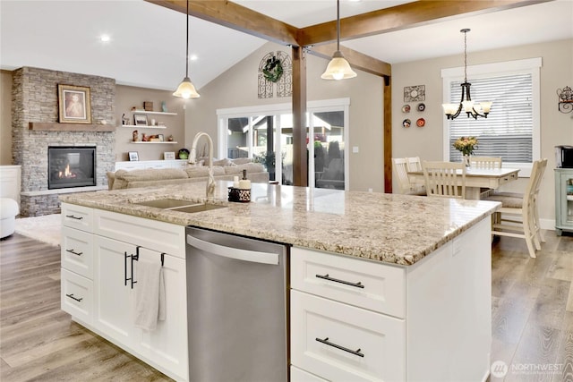 kitchen with stainless steel dishwasher, a stone fireplace, a healthy amount of sunlight, and a sink