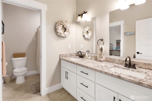 bathroom with a sink, baseboards, toilet, and double vanity