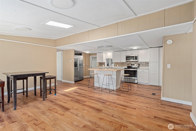 kitchen featuring white cabinetry, a kitchen breakfast bar, light wood-style floors, and appliances with stainless steel finishes