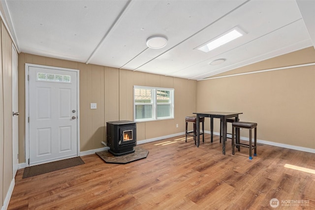 interior space with vaulted ceiling, a wood stove, baseboards, and wood finished floors