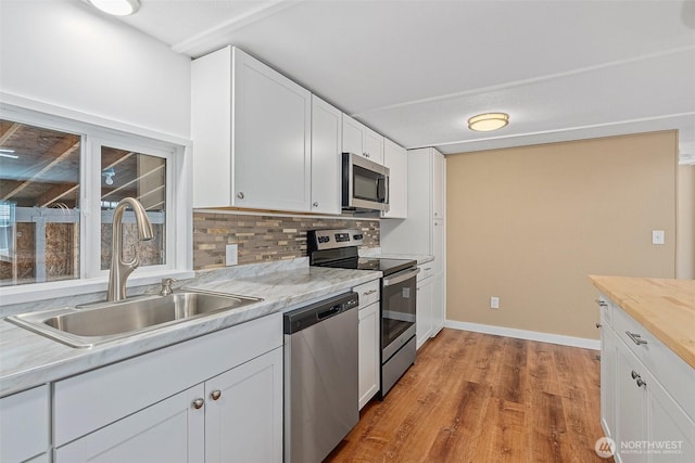 kitchen featuring light wood-type flooring, a sink, stainless steel appliances, white cabinets, and decorative backsplash