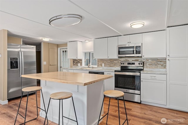 kitchen featuring a sink, appliances with stainless steel finishes, wood counters, a kitchen bar, and light wood-type flooring