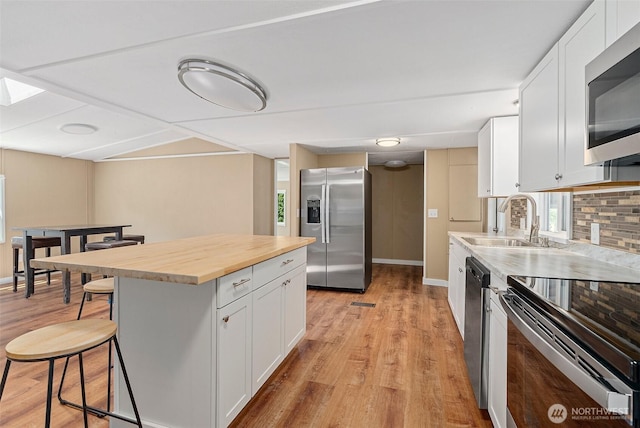 kitchen with a sink, butcher block countertops, stainless steel appliances, white cabinetry, and a kitchen breakfast bar