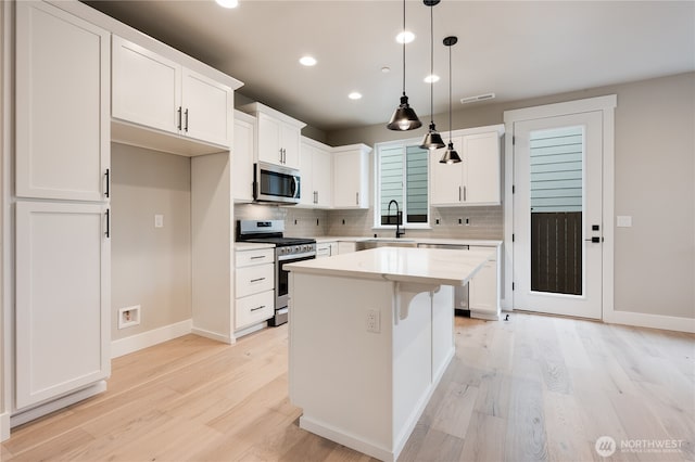 kitchen with white cabinets, stainless steel appliances, light wood-style flooring, and a sink