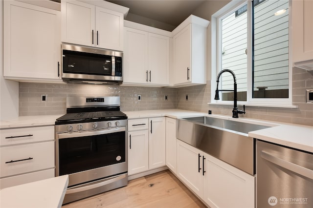 kitchen featuring a sink, stainless steel appliances, backsplash, and white cabinetry