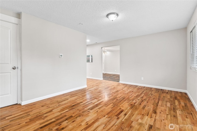 empty room featuring light wood-style floors, baseboards, and a textured ceiling