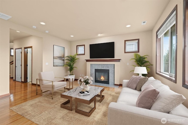 living room with visible vents, baseboards, a fireplace with flush hearth, recessed lighting, and light wood-style floors