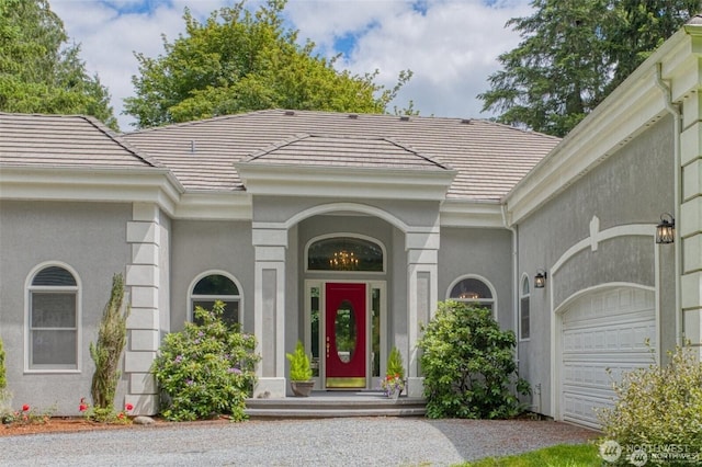 entrance to property with a tiled roof, stucco siding, and an attached garage