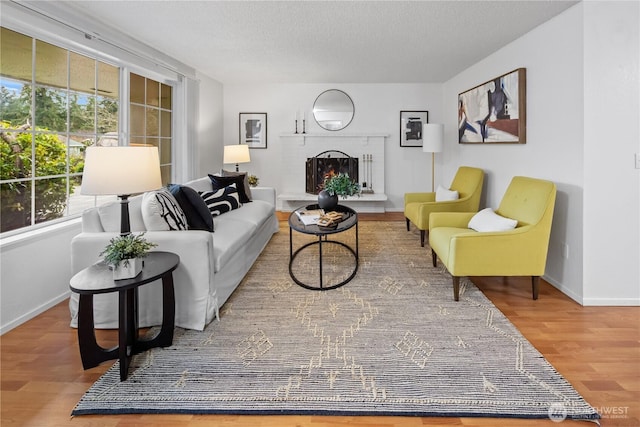 living room with a brick fireplace, wood finished floors, baseboards, and a textured ceiling