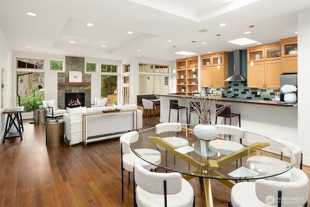 dining area with a tray ceiling, recessed lighting, dark wood-style floors, and a large fireplace