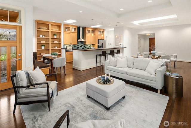 living room featuring baseboards, a skylight, recessed lighting, dark wood-type flooring, and a raised ceiling