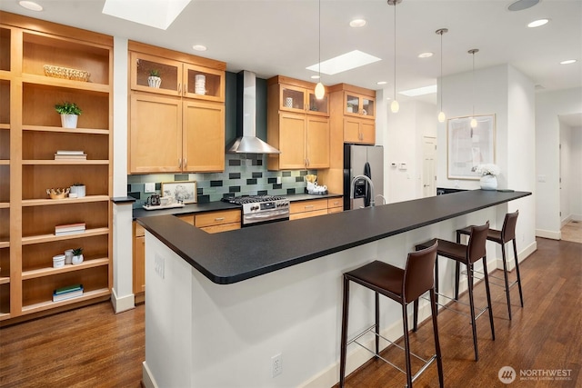 kitchen with dark countertops, appliances with stainless steel finishes, a skylight, and wall chimney range hood