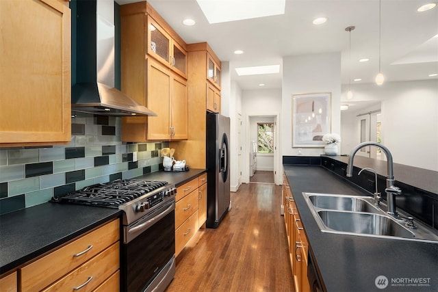 kitchen with dark countertops, stainless steel gas range, wall chimney exhaust hood, and a sink