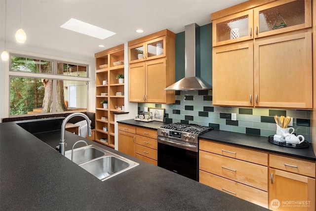 kitchen with dark countertops, stainless steel range with gas stovetop, wall chimney range hood, and a sink