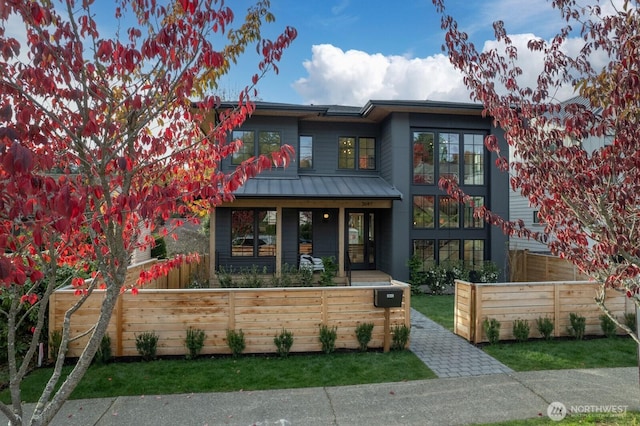 view of front facade with a standing seam roof, covered porch, a fenced front yard, and metal roof