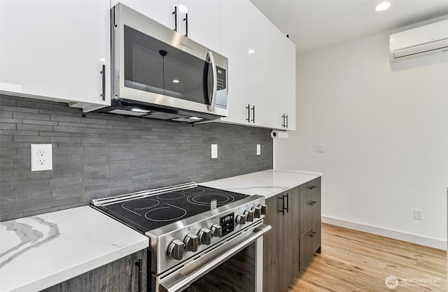 kitchen with light wood-type flooring, a wall mounted AC, white cabinetry, stainless steel appliances, and light stone countertops