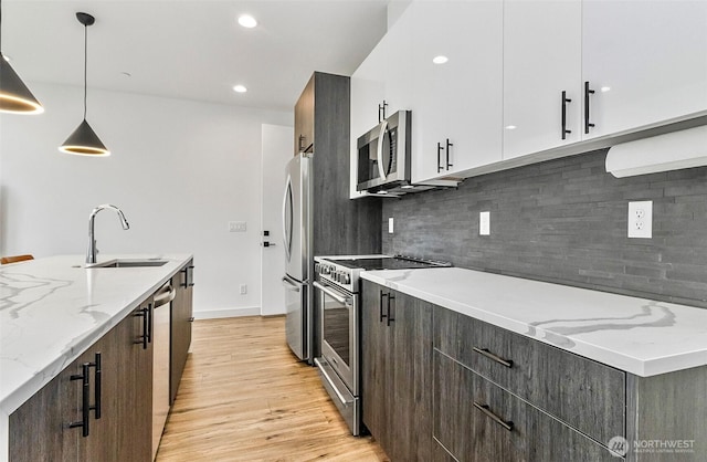 kitchen featuring decorative light fixtures, light wood-type flooring, appliances with stainless steel finishes, modern cabinets, and a sink