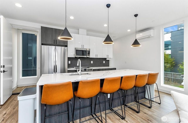 kitchen with an AC wall unit, appliances with stainless steel finishes, decorative backsplash, and a healthy amount of sunlight