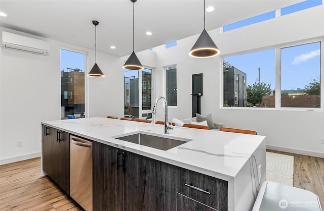 kitchen with a wall mounted air conditioner, an island with sink, light wood-style floors, and a sink