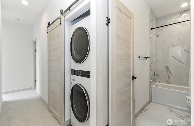 laundry area featuring stacked washer / dryer, marble finish floor, baseboards, and a barn door