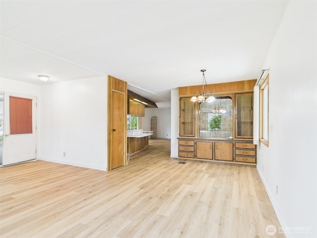 kitchen featuring brown cabinetry, baseboards, light wood finished floors, pendant lighting, and a chandelier