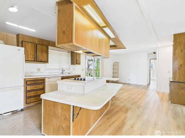 kitchen with white appliances, a kitchen island, a sink, light countertops, and light wood-type flooring