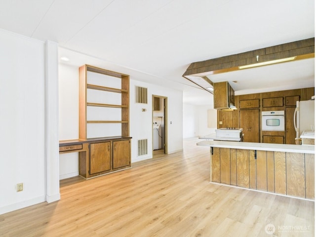 kitchen featuring brown cabinetry, visible vents, white appliances, and light wood-style floors