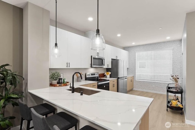 kitchen featuring a peninsula, a sink, stainless steel appliances, a kitchen bar, and light wood-type flooring