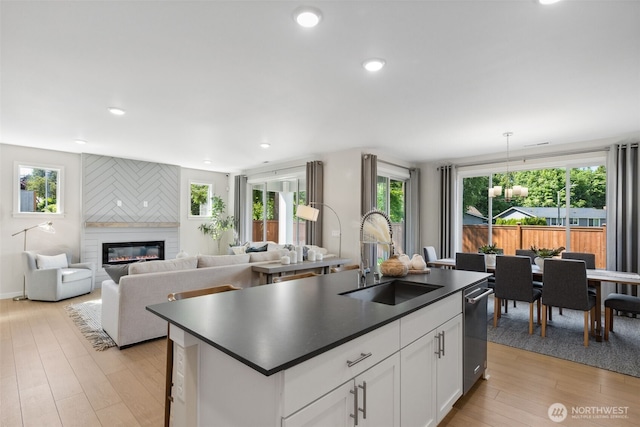 kitchen featuring light wood-style flooring, a sink, dark countertops, a large fireplace, and a healthy amount of sunlight