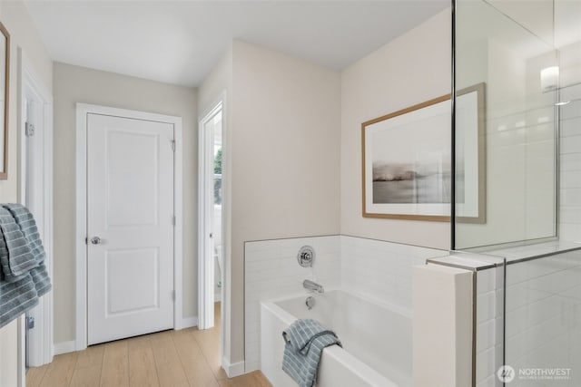 full bath featuring baseboards, a garden tub, and wood finished floors