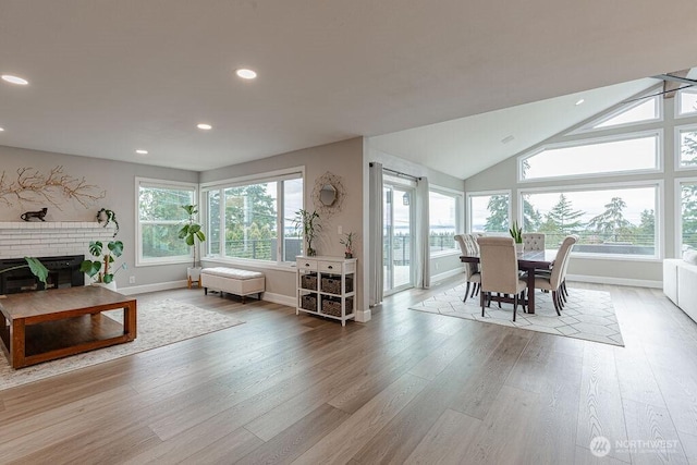 living area featuring wood finished floors, recessed lighting, baseboards, a brick fireplace, and vaulted ceiling