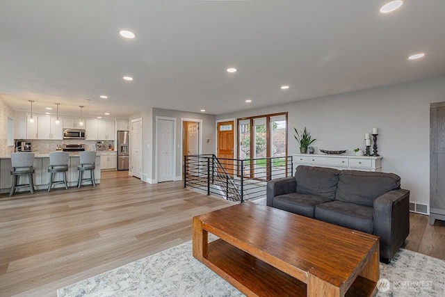 living room with light wood finished floors, visible vents, recessed lighting, and baseboards