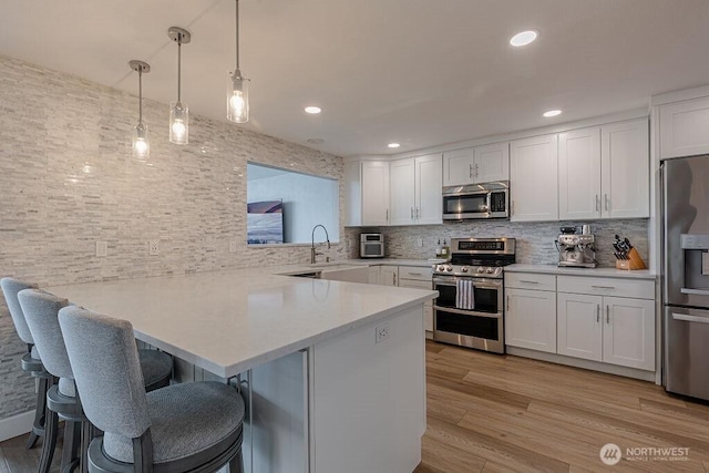 kitchen featuring a kitchen bar, light countertops, appliances with stainless steel finishes, a peninsula, and white cabinetry