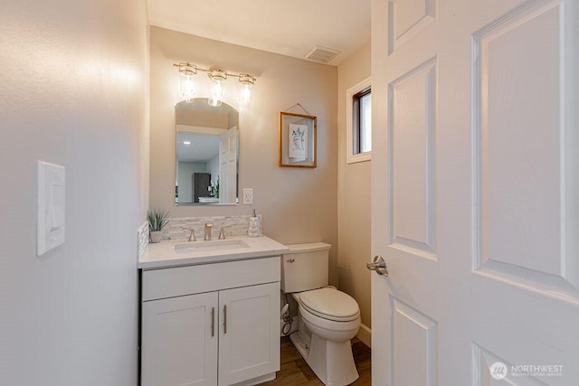 half bath with visible vents, toilet, wood finished floors, and vanity