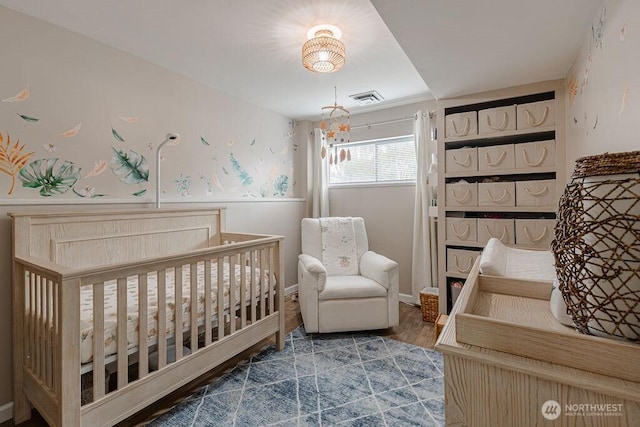 bedroom featuring visible vents, a nursery area, wood finished floors, and a chandelier