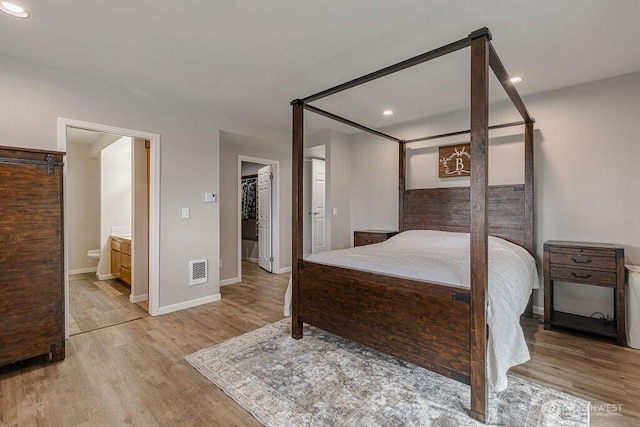 bedroom featuring wood finished floors, visible vents, recessed lighting, a walk in closet, and connected bathroom