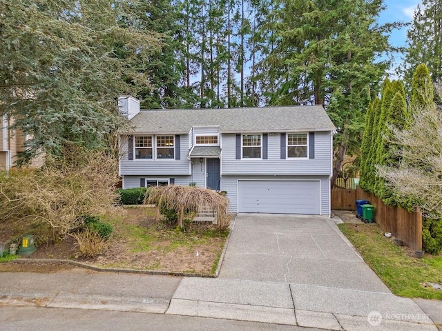 split foyer home with fence, roof with shingles, driveway, a chimney, and a garage