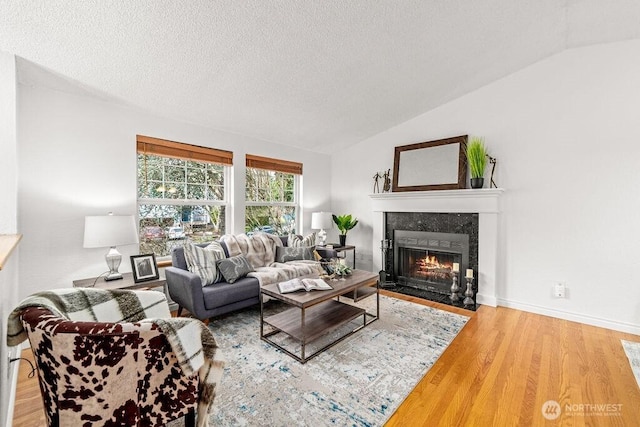 living area with lofted ceiling, a fireplace with flush hearth, wood finished floors, and a textured ceiling