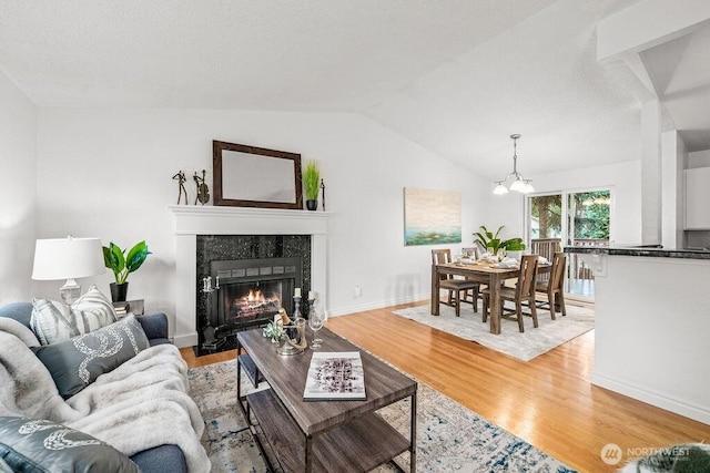 living room featuring light wood-style flooring, baseboards, lofted ceiling, a chandelier, and a tile fireplace