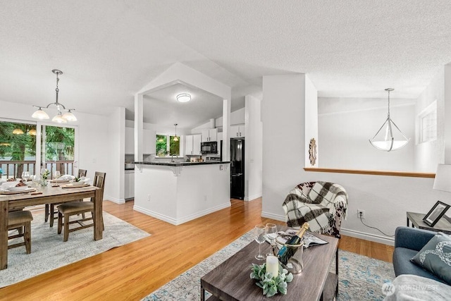 living room with baseboards, a textured ceiling, light wood-style flooring, and vaulted ceiling