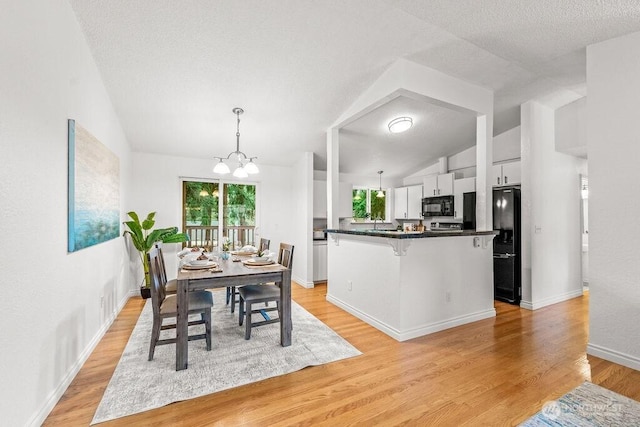 dining room with light wood-type flooring, lofted ceiling, a notable chandelier, and a textured ceiling