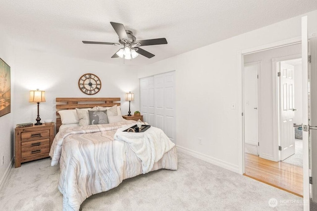 bedroom with a ceiling fan, baseboards, a closet, a textured ceiling, and light carpet