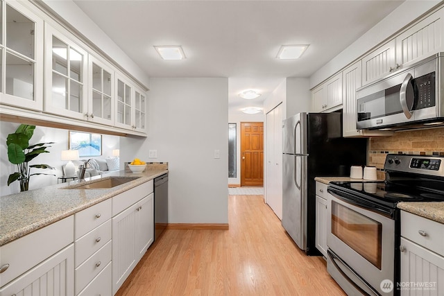 kitchen with light wood-type flooring, a sink, stainless steel appliances, glass insert cabinets, and tasteful backsplash