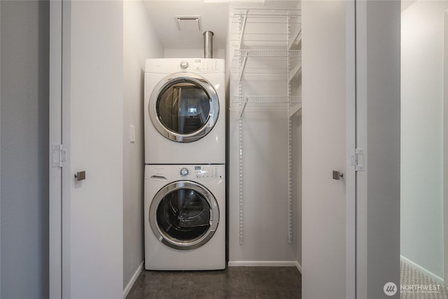 clothes washing area with visible vents, baseboards, stacked washer and clothes dryer, and laundry area