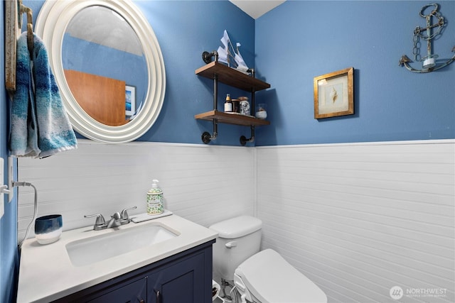 half bath with vanity, toilet, and wainscoting