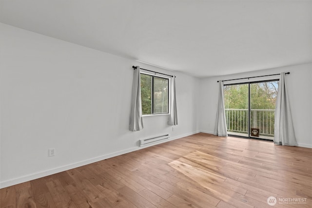 empty room with a baseboard heating unit, plenty of natural light, baseboards, and light wood finished floors