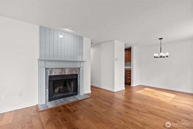 unfurnished living room featuring a notable chandelier, a fireplace, baseboards, and hardwood / wood-style flooring