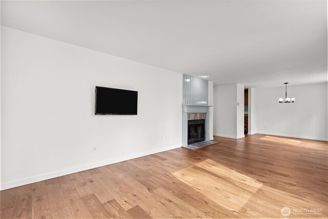 unfurnished living room featuring light wood finished floors, a notable chandelier, a fireplace, and baseboards