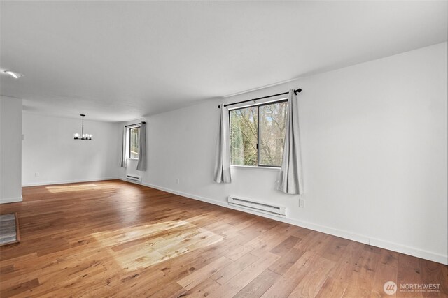 spare room featuring hardwood / wood-style floors, baseboards, an inviting chandelier, a baseboard heating unit, and baseboard heating