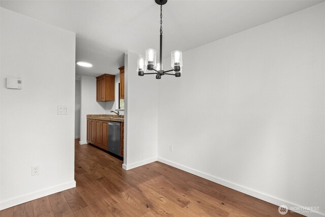 unfurnished dining area featuring a notable chandelier, baseboards, and dark wood-type flooring